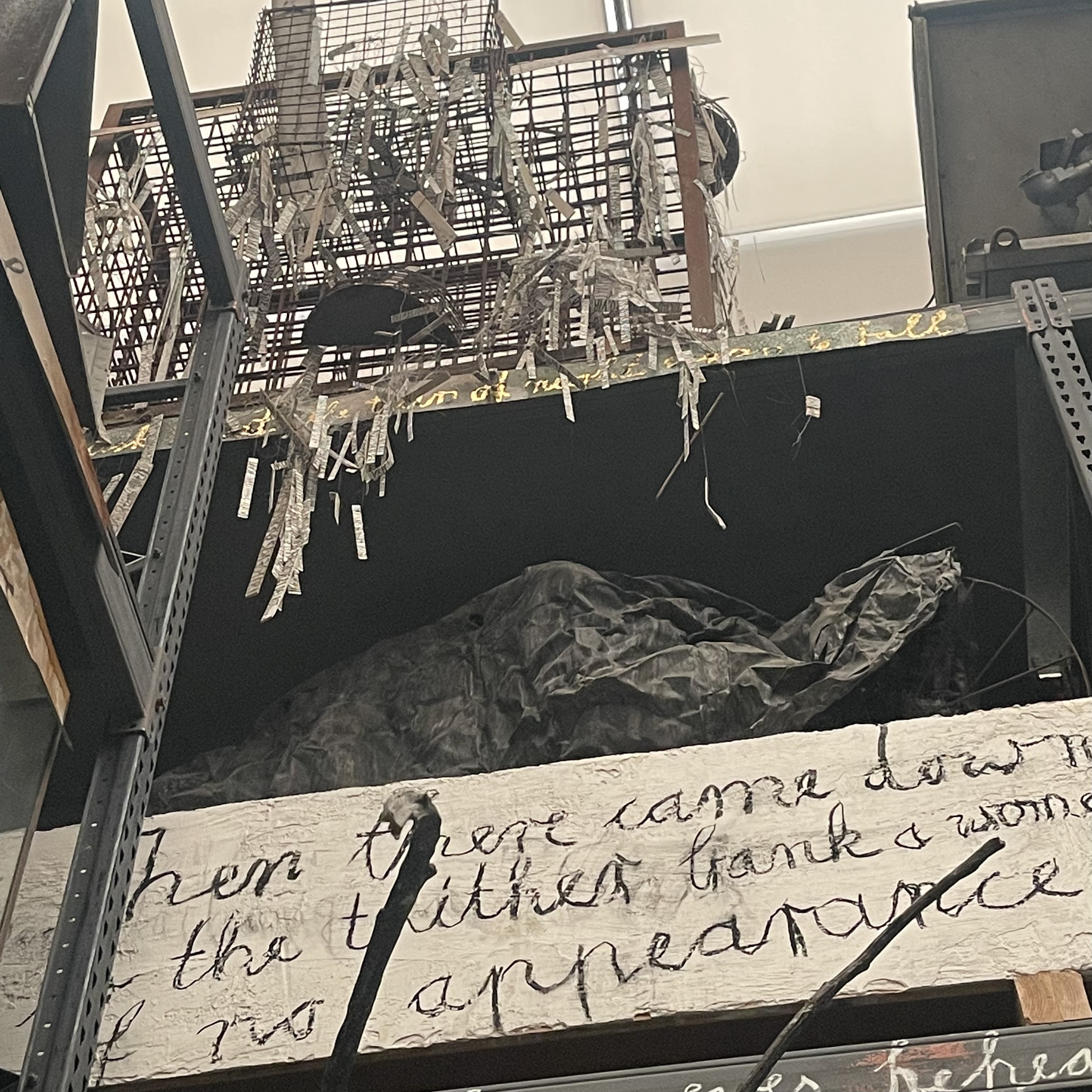 Handwritten words on a board beneath a wire cage of shredded paper, in a Bermondsey gallery