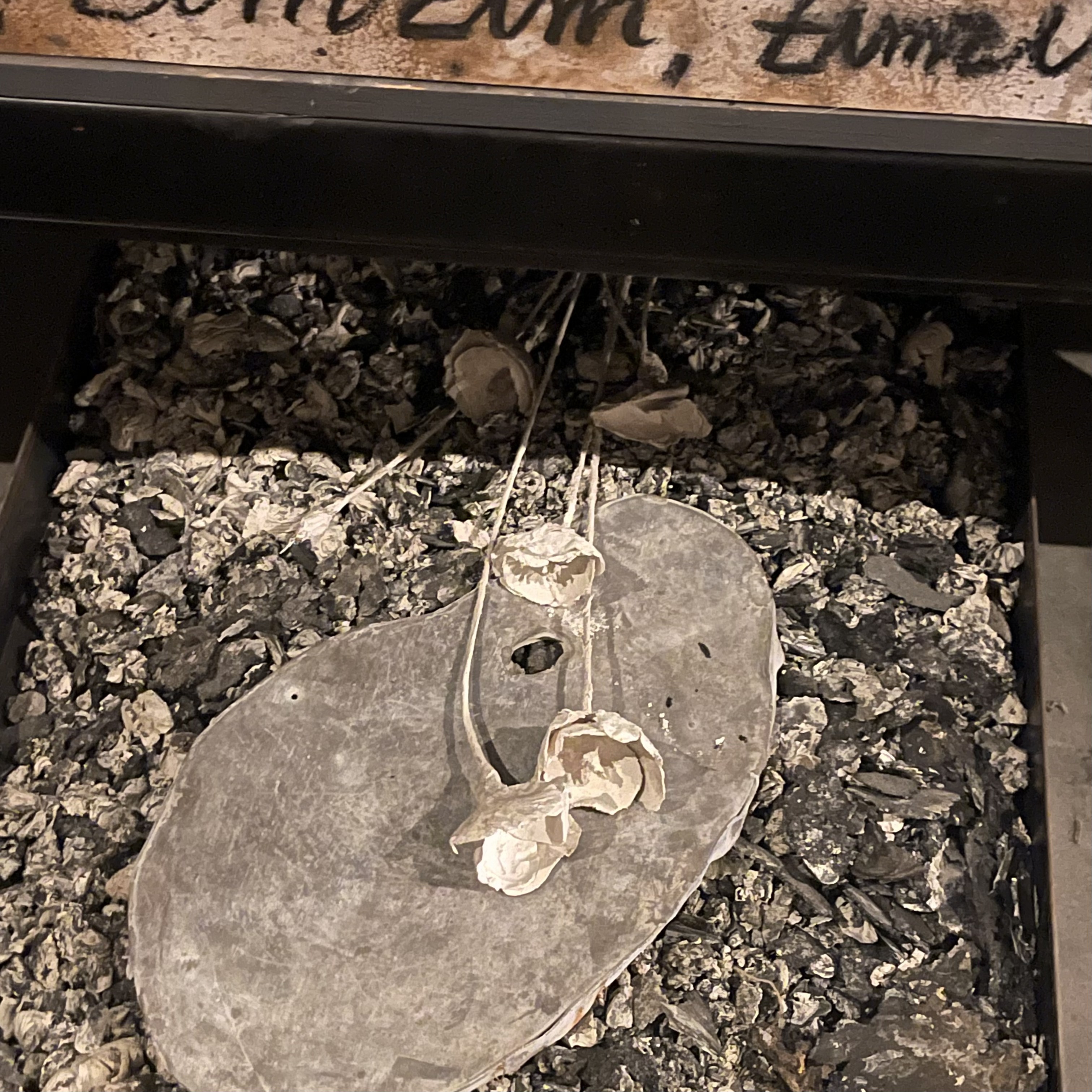 A grey palette shape and wire flowers resting on a bed of ash, in a Bermondsey gallery