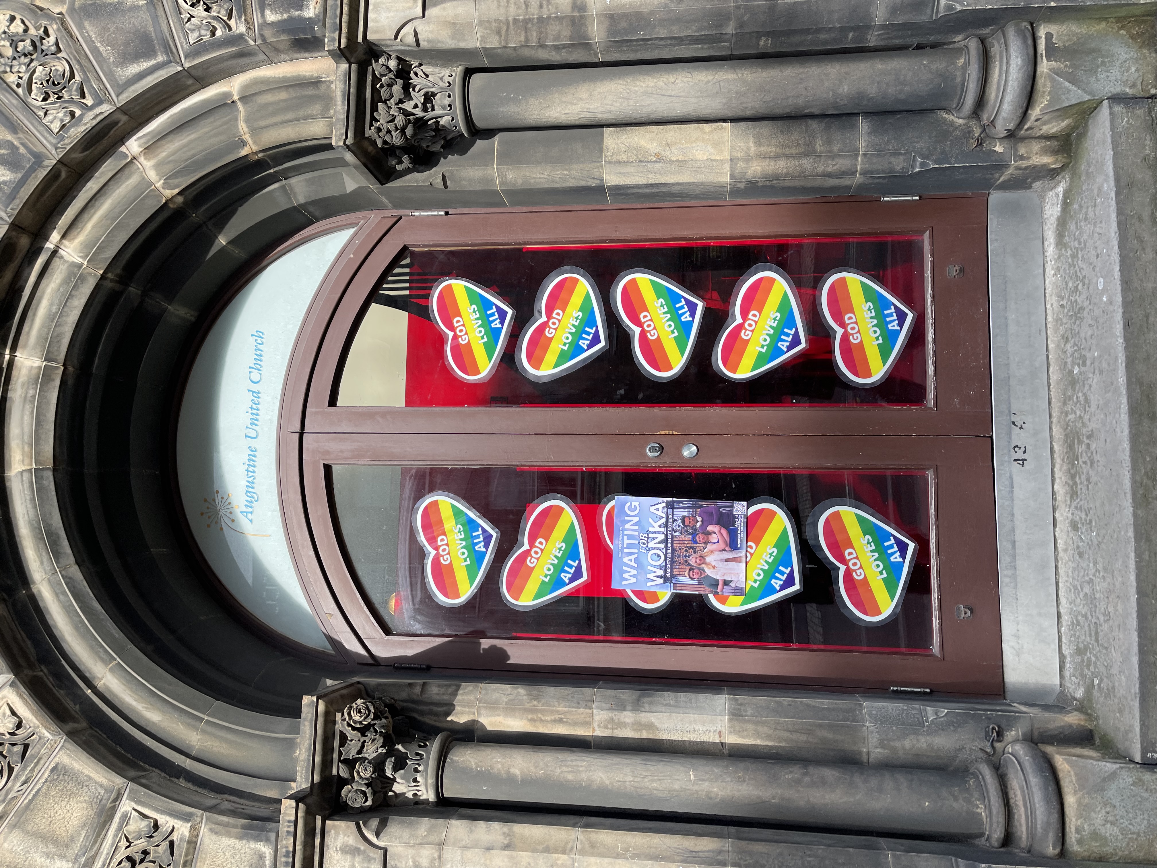 An arched stone doorway in Edinburgh with red doors covered in rainbow heart posters
