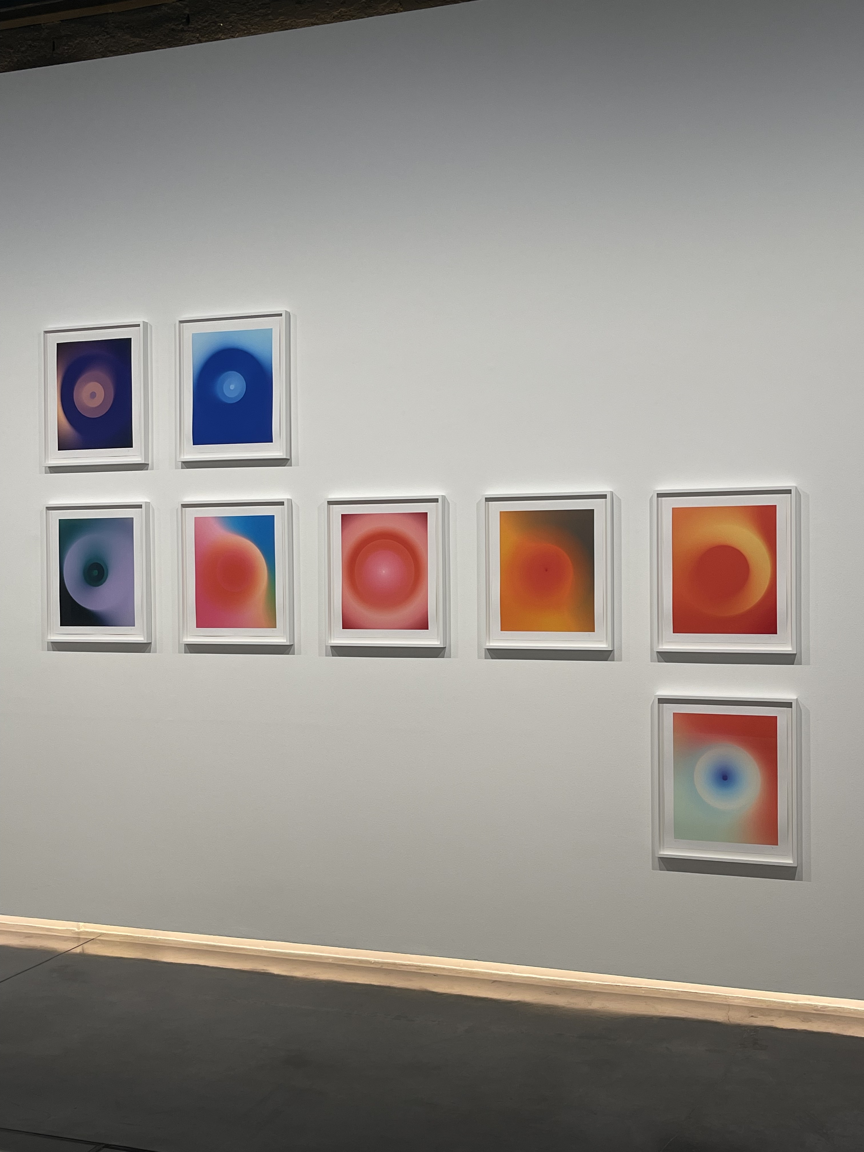 A grid of framed prints of glowing blue, red and orange circles on a white gallery wall