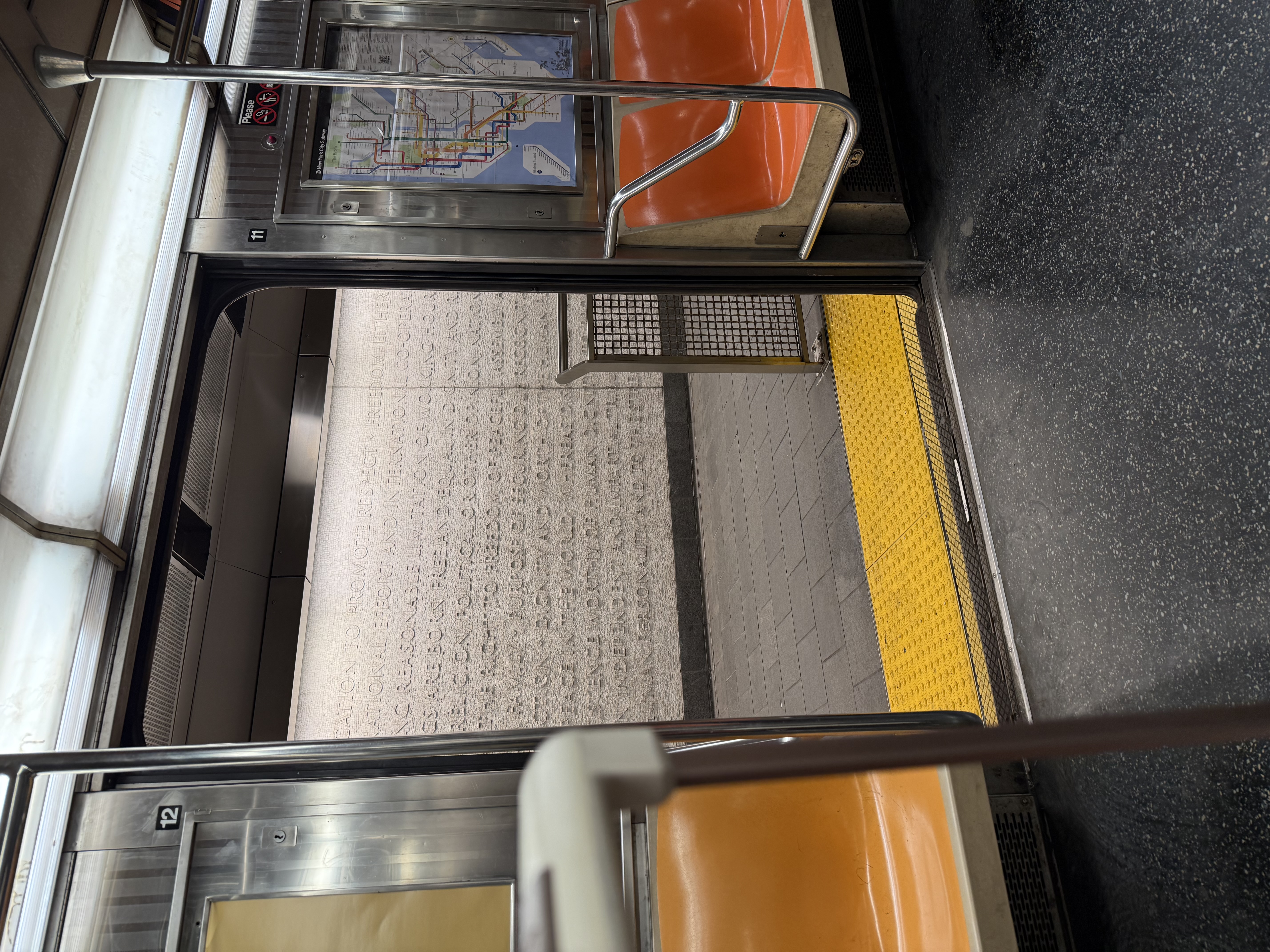 Open subway car doors at WTC Cortlandt station, with orange seats and a white wall of carved text beyond