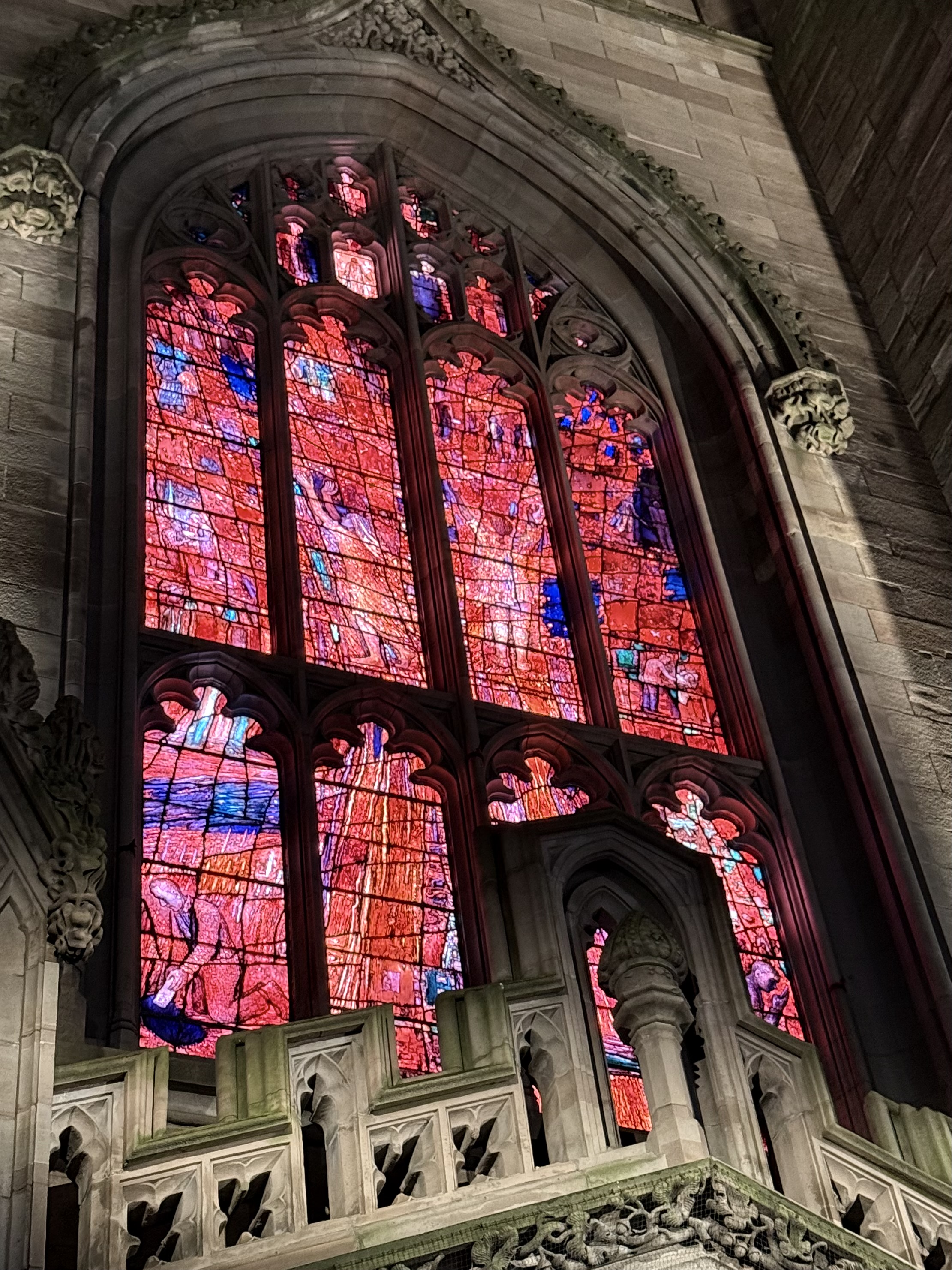 A tall stained glass window glowing red inside Trinity Church in New York