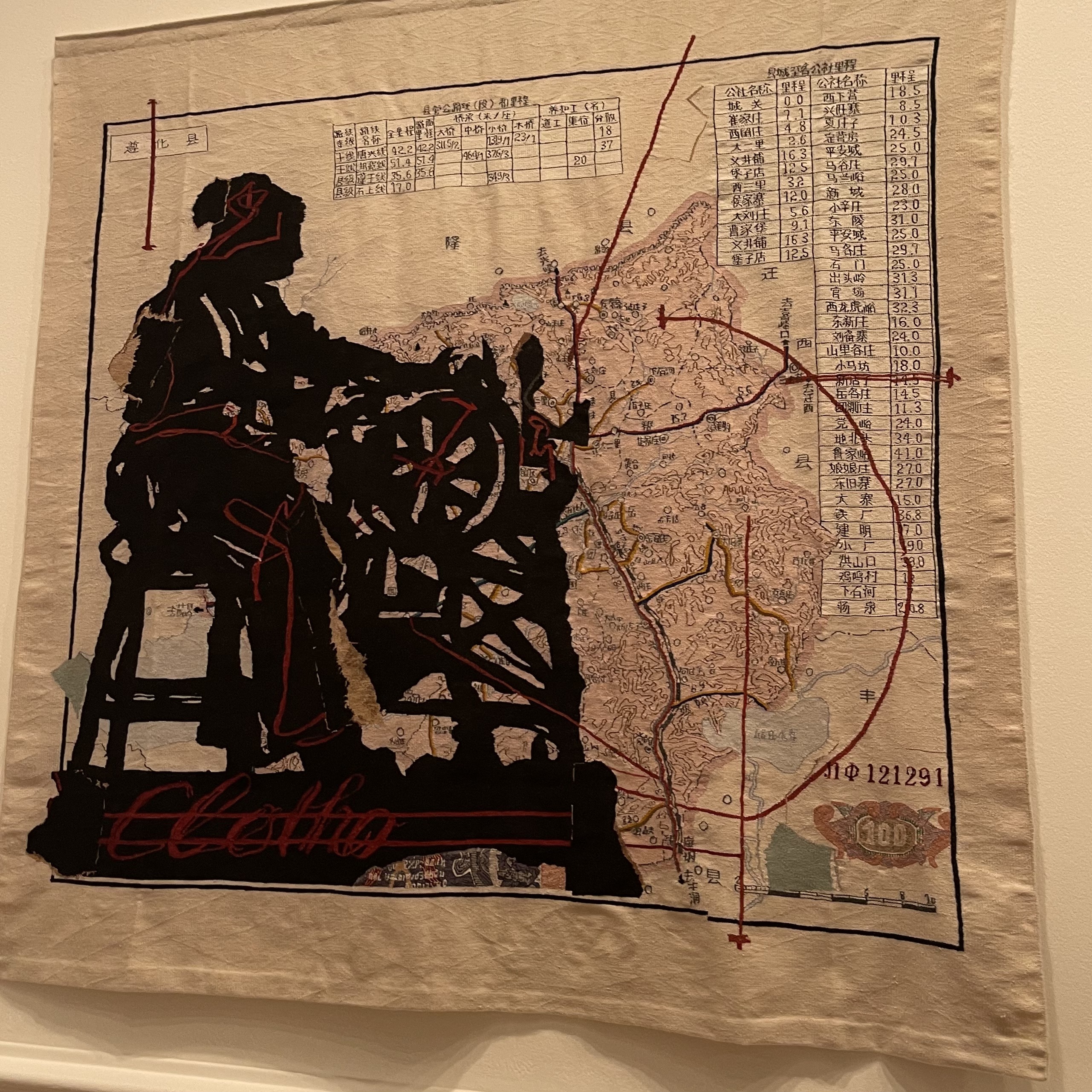 A large embroidered tapestry at the Royal Academy: a black silhouette of a woman at a spinning wheel over a hand-drawn map