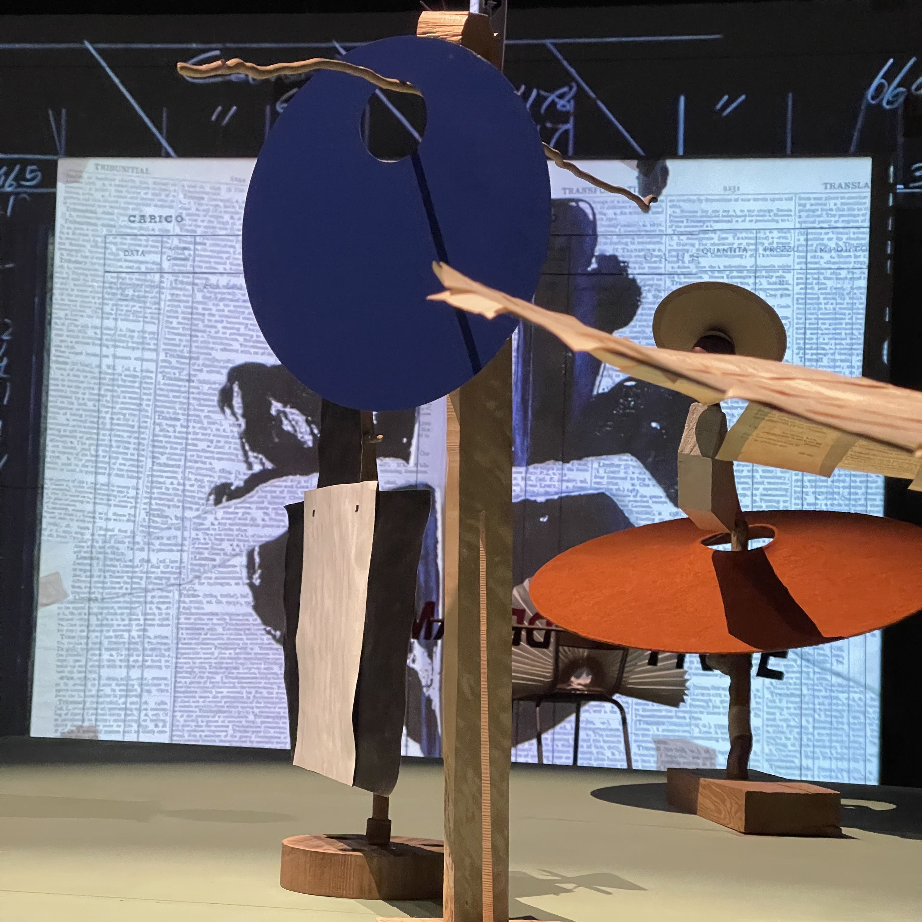 Cut-out props on wooden stands in front of a projected page of handwritten records at the Royal Academy