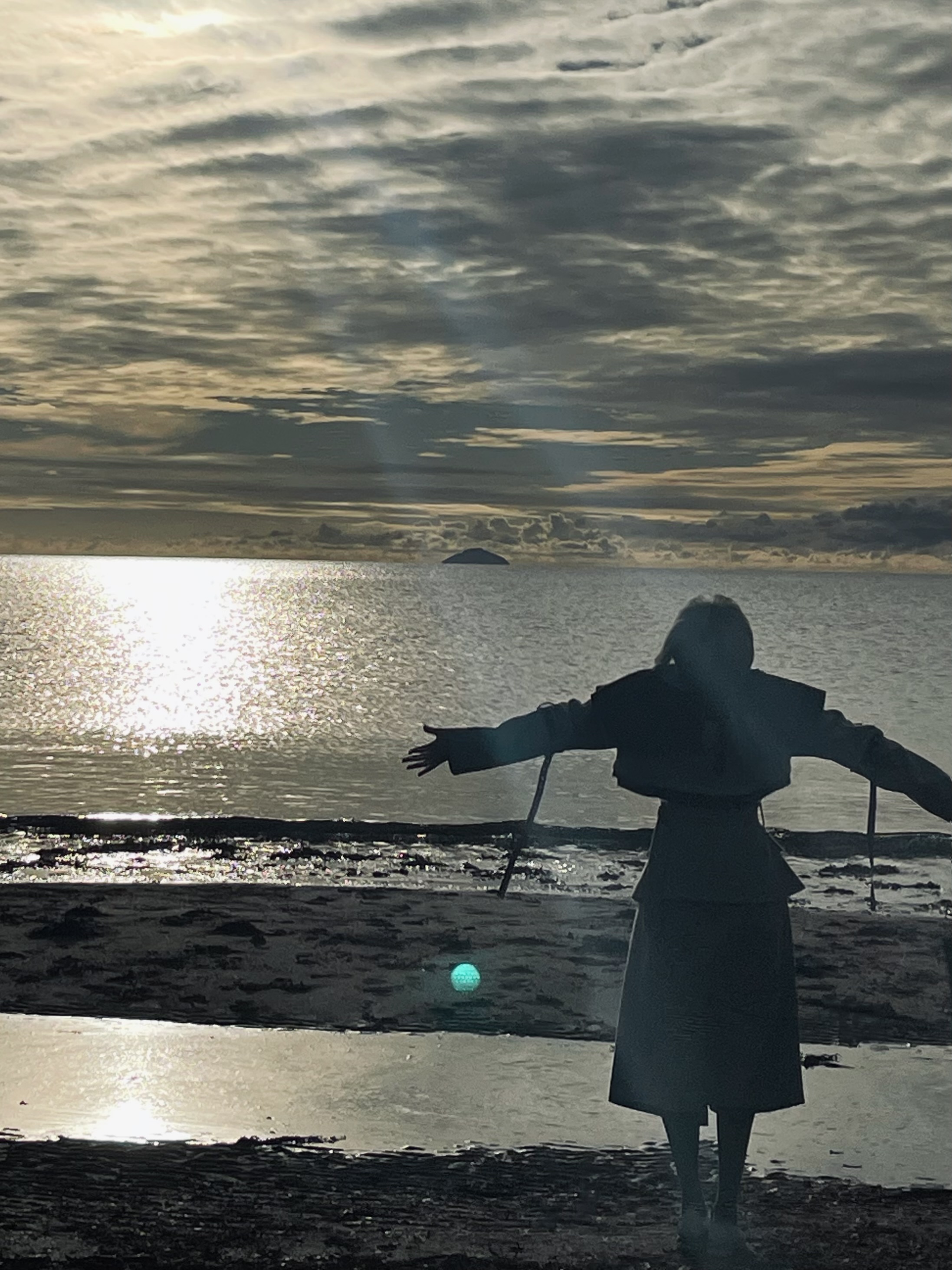 A silhouette of a person with arms outstretched on the beach at Troon, the sun low over the water