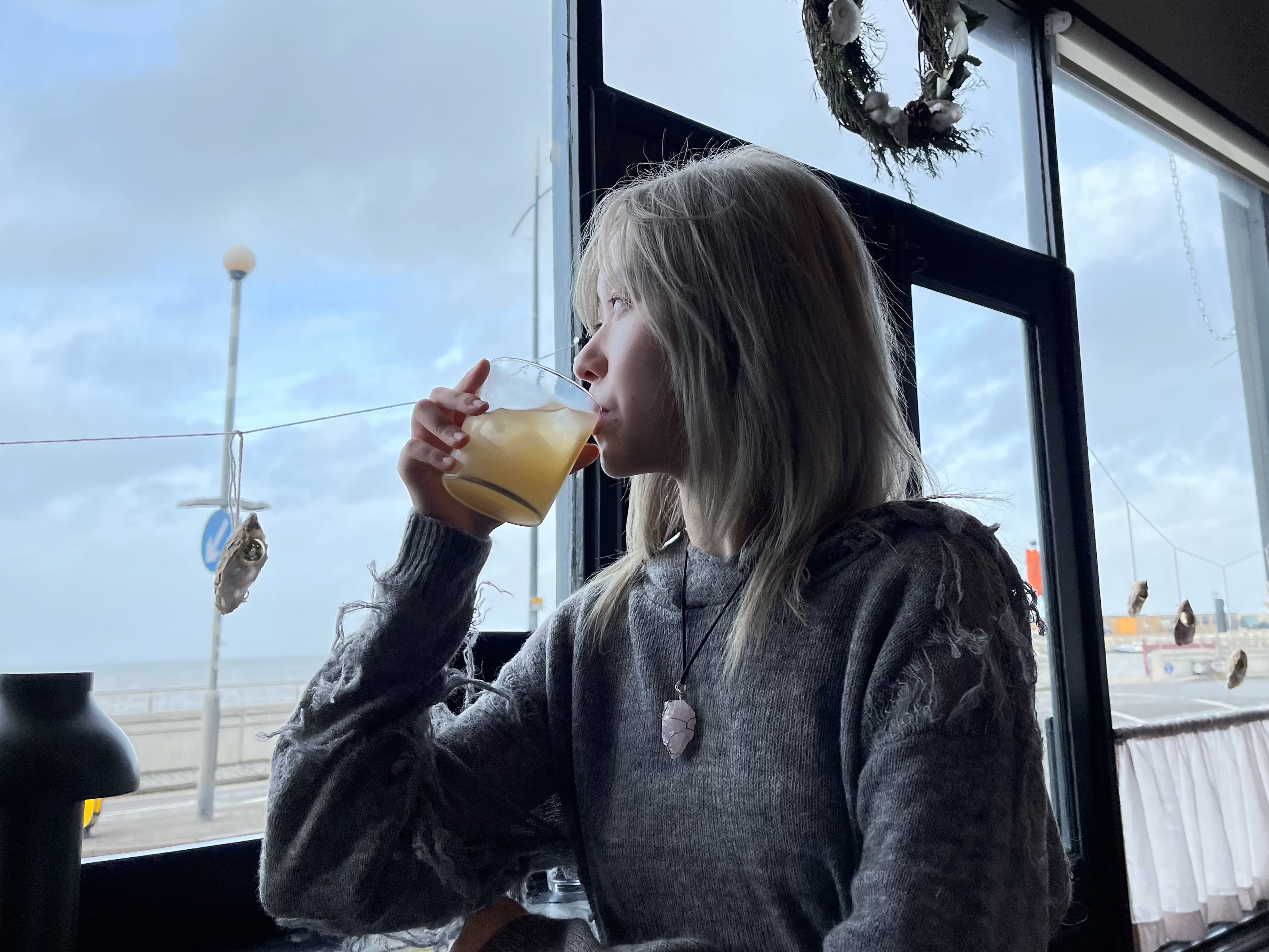 Violet sipping a drink by a window looking out over the seafront in Margate
