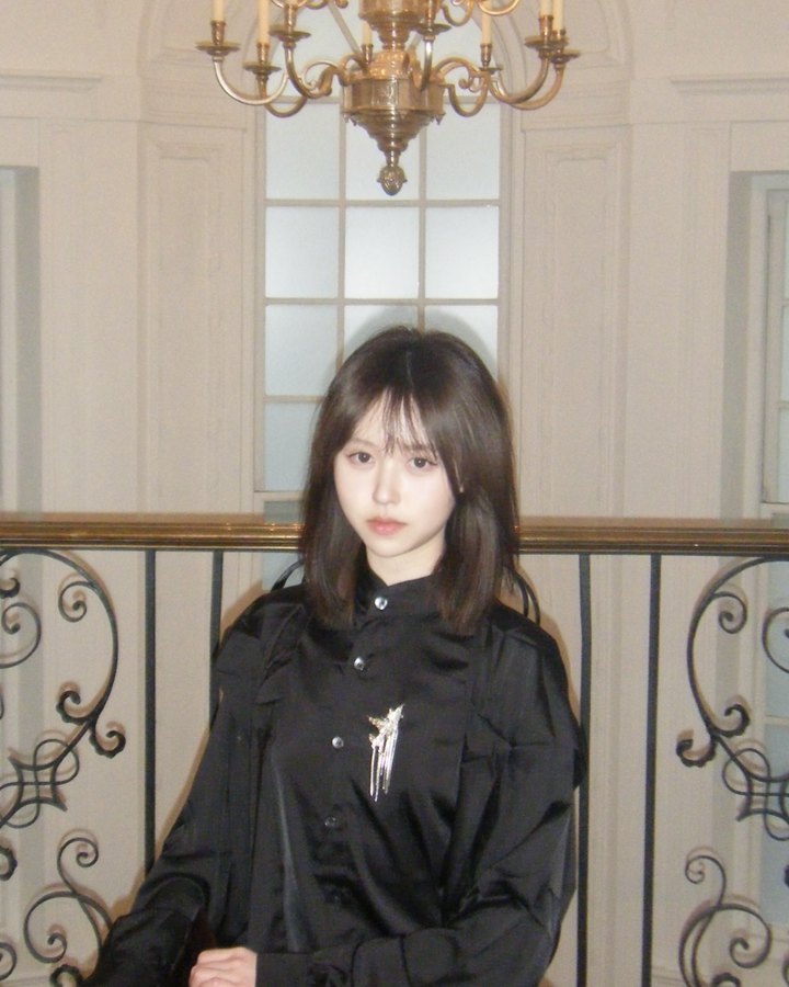 Portrait of Violet in a black shirt, seated beneath a candle chandelier by a wrought-iron balustrade